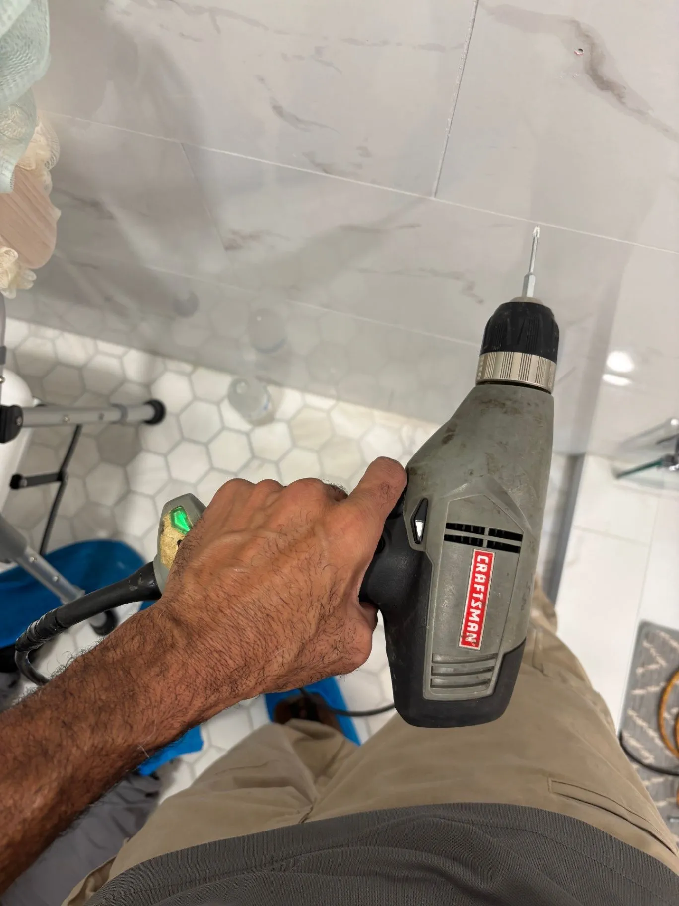 Authentic installation detail showing a hand drilling into a tiled shower wall
