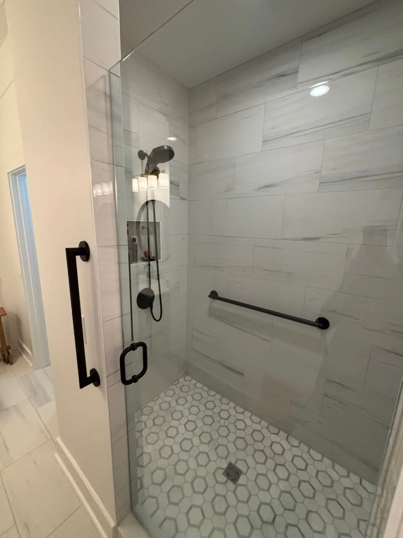 Close view of black shower hardware and a horizontal grab bar beside a glass shower enclosure.