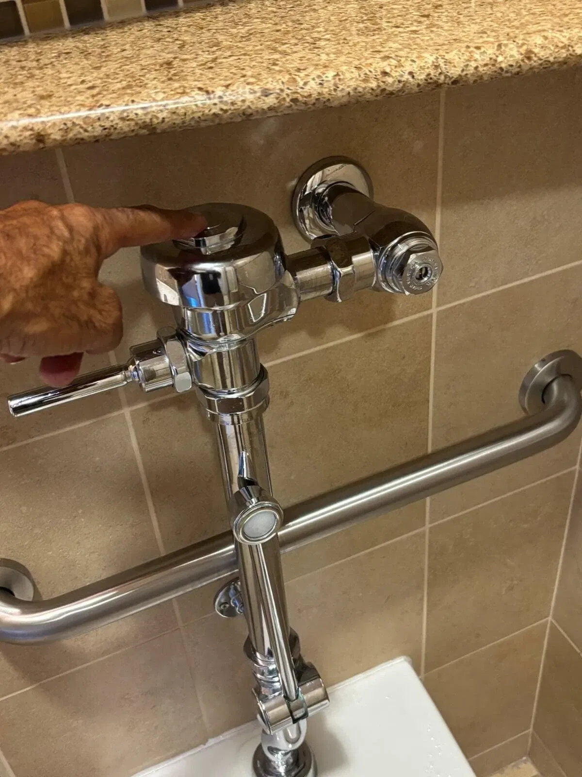Technician inspecting a chrome commercial flush valve as an example of facility service work
